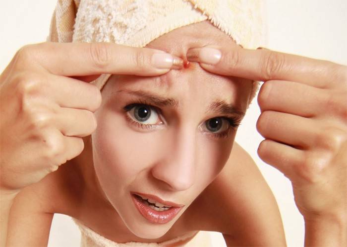 La muchacha aprieta un grano en su cara.