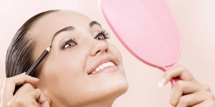 Fille avec un miroir dans la main peint les sourcils avec un crayon
