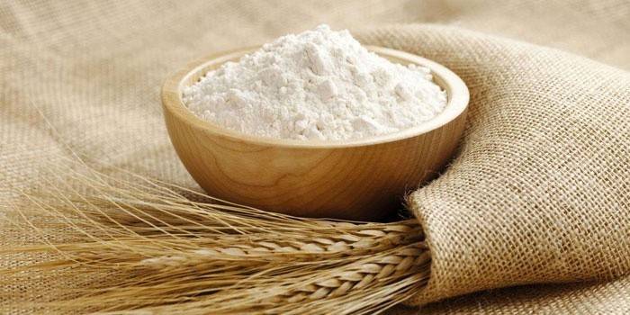 Farinha em uma tigela de madeira e espigas de trigo