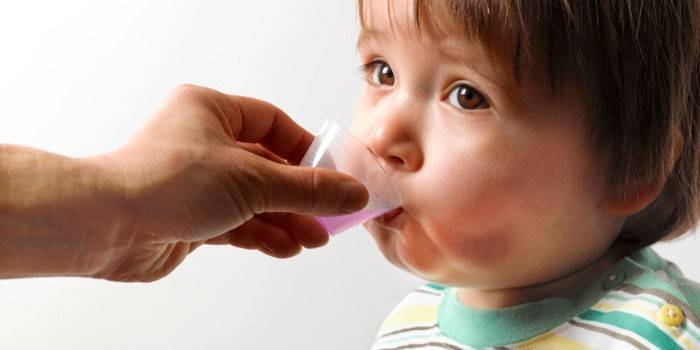 El niño recibe medicamentos en una taza medidora.