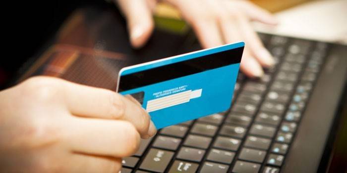 Meitene klēpjdatora priekšā ar bankas karti rokā