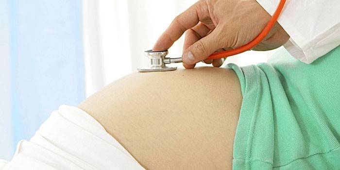 Medicul asculta bătăile inimii fetale din abdomenul unei femei însărcinate