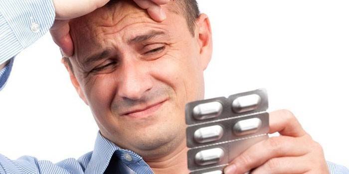 Một người đàn ông bị đau đầu cầm một vỉ thuốc trong tay