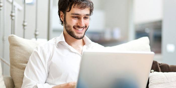 Um homem se senta em um sofá com um laptop