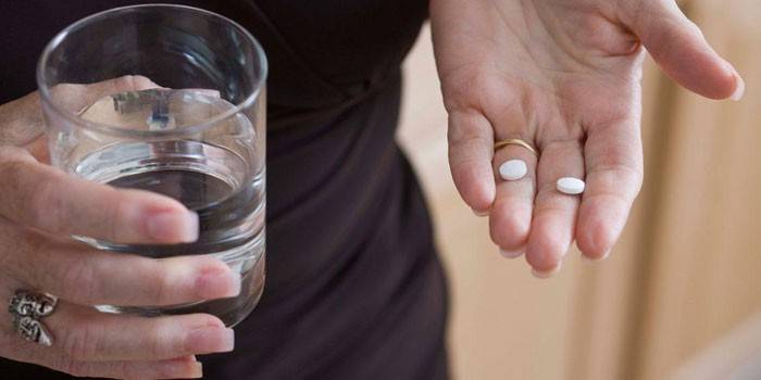 Frau hält Pillen und ein Glas Wasser in ihren Händen