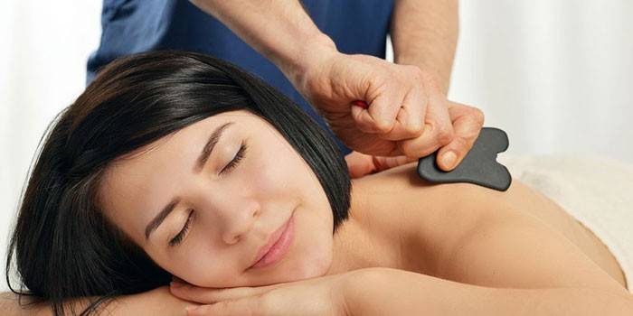 Masseur effectue un massage avec un grattoir Guasha