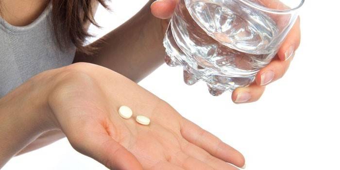 Pillen auf einer Handfläche und einem Glas Wasser