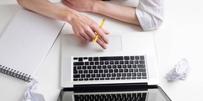Ember egy laptop, egy ceruza a kezében és egy notebook