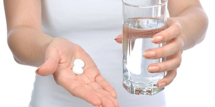 Pilules et un verre d'eau dans les mains d'une fille