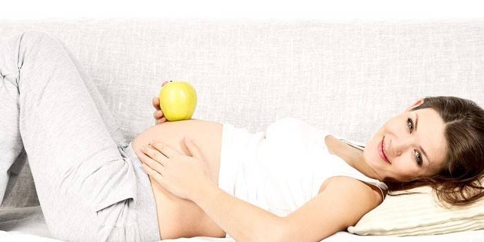 Das schwangere Mädchen liegt auf einem Sofa und hält einen Apfel in der Hand