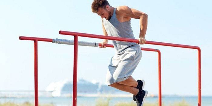 Un homme effectue des tractions sur les barres asymétriques.