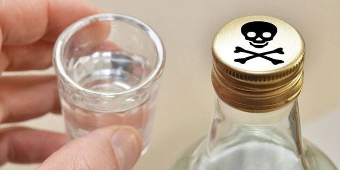Sticlă de alcool cu ​​un semn de otravă pe capac și un pahar în mână