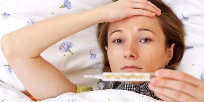 Das Mädchen liegt mit einem Thermometer in der Hand im Bett