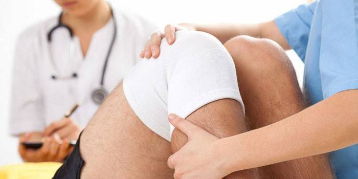 Medicul îi pune pacientului o compresă pe genunchi