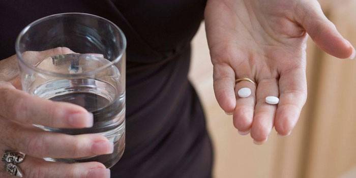 Pillole sul palmo e un bicchiere d'acqua in mano