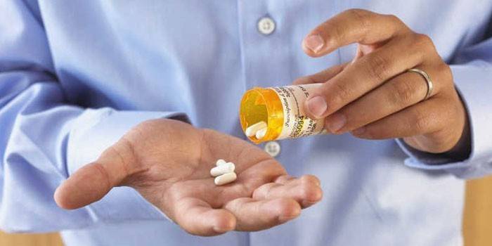 El hombre sostiene un frasco y pastillas en sus manos