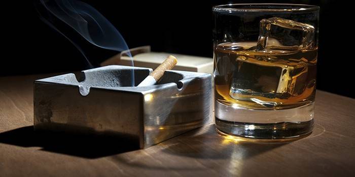 Ένα τσιγάρο που τρώει σε ένα τασάκι και ένα ποτήρι αλκοόλ