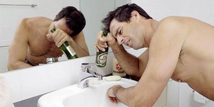 Hombre en el baño con una botella de cerveza en la mano.