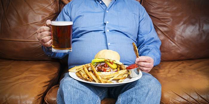 Uomo grasso con una birra e cibo spazzatura