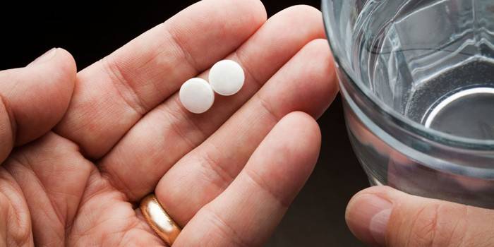 Một người đàn ông cầm trong tay hai viên thuốc và một ly nước