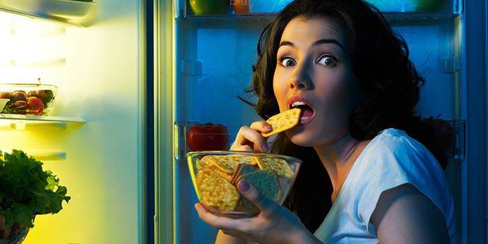 Cô gái ăn bánh quy trước tủ lạnh mở