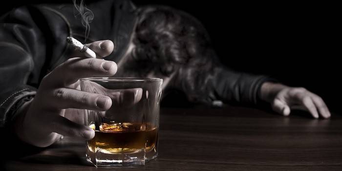 Un uomo dorme su un tavolo con una sigaretta e un bicchiere di alcol in mano