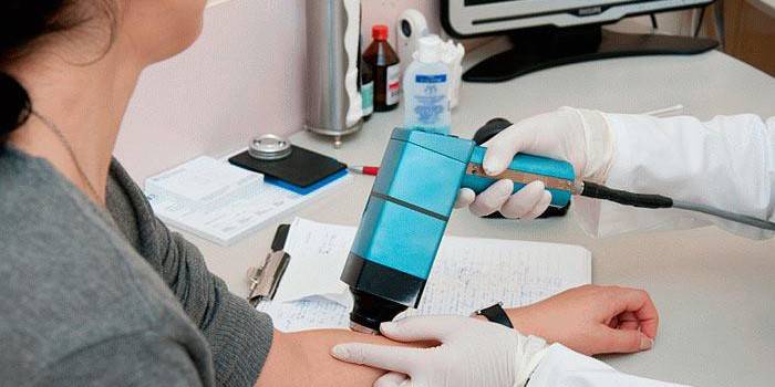 Gydytojas atlieka epiluminescencinę paciento odos dermatoskopiją
