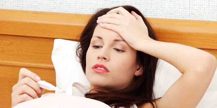 Eine Frau liegt im Bett und schaut auf ein Thermometer