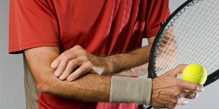 Mann mit einem Tennisschläger hält seinen Ellbogen.