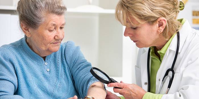 O médico examina a mão do paciente com uma lupa.