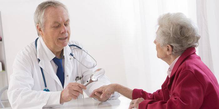 Der Arzt untersucht die Hand des Patienten durch eine Lupe.