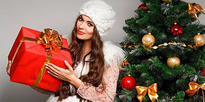 Mergaitė šalia Naujųjų Metų medžio su dovana