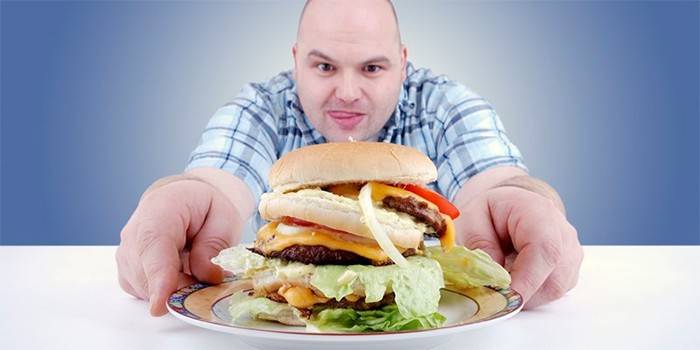 Apaļš vīrietis tiecas pēc hamburgera uz šķīvja