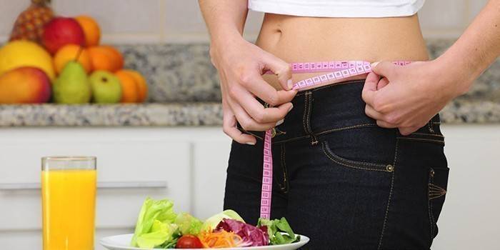 Centímetro em uma cintura feminina, salada de legumes e suco
