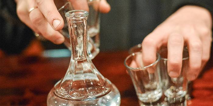 O carafă cu vodcă și ochelari în mâna unui bărbat