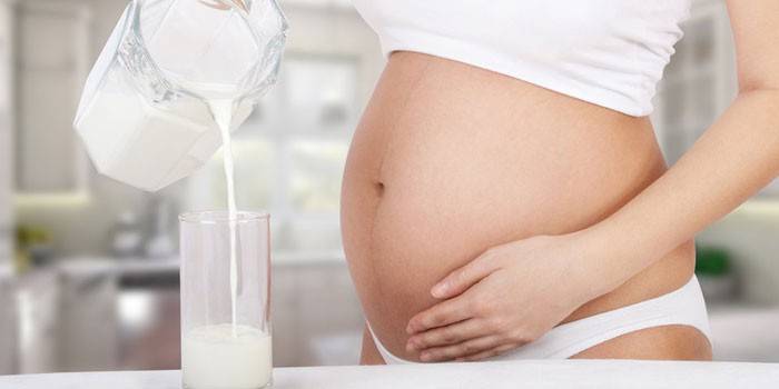 Schwangere Frau gießt gegorene gebackene Milch in ein Glas